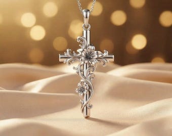 May include: A silver-toned metal cross pendant suspended from a matching chain. The cross features intricate, raised floral and vine-like scrollwork detailing that wraps around the vertical and horizontal bars of the cross structure.