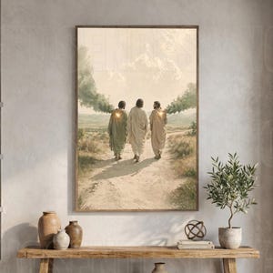 Puede incluir: Una impresión artística enmarcada que muestra a tres figuras con túnicas caminando por un sendero de tierra en un paisaje. La escena presenta tonos tierra suaves y apagados, nubes ligeras y un cielo brillante sobre un banco de madera.