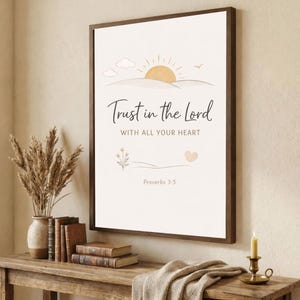 Puede incluir: Un cuadro decorativo con un sol, nubes y un icono de corazón con el texto Trust in the Lord WITH ALL YOUR HEART Proverbs 3:5. El diseño utiliza tonos beige y amarillos suaves sobre un fondo blanco, presentado en un marco de madera oscura.