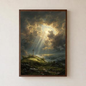 Puede incluir: Pintura de paisaje enmarcada que representa una cruz sobre una colina, bañada por la luz solar que atraviesa nubes oscuras y dramáticas. La obra de arte presenta un camino que conduce a la cruz, con una cualidad serena y etérea. El marco es de color marrón oscuro.