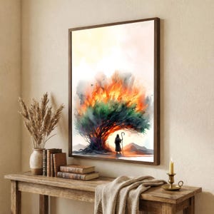 Puede incluir: Una lámina de arte mural enmarcada que presenta una ilustración en acuarela de una figura de pie ante un gran árbol en llamas con vibrantes tonos naranjas, amarillos y verdes. La escena se sitúa sobre un fondo pálido con siluetas de montañas.