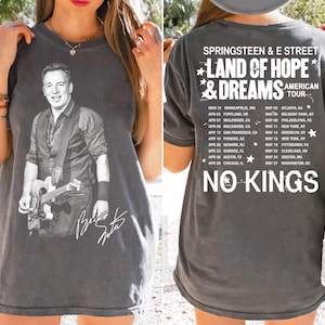 May include: Gray t-shirt featuring a black and white image of a musician playing a guitar, with his signature. The back of the shirt displays tour dates and the text "SPRINGSTEEN & E STREET LAND OF HOPE & DREAMS AMERICAN TOUR". The words "NO KINGS" are also printed on the back.
