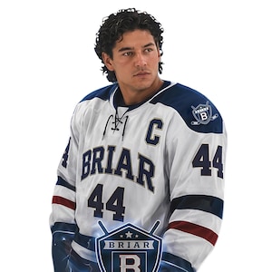 Puede incluir: Una camiseta de hockey blanca y azul marino con la palabra "BRIAR" en letras grandes en el pecho y el número "44" en las mangas. La camiseta tiene una "C" de capitán y un logotipo del equipo en el hombro.