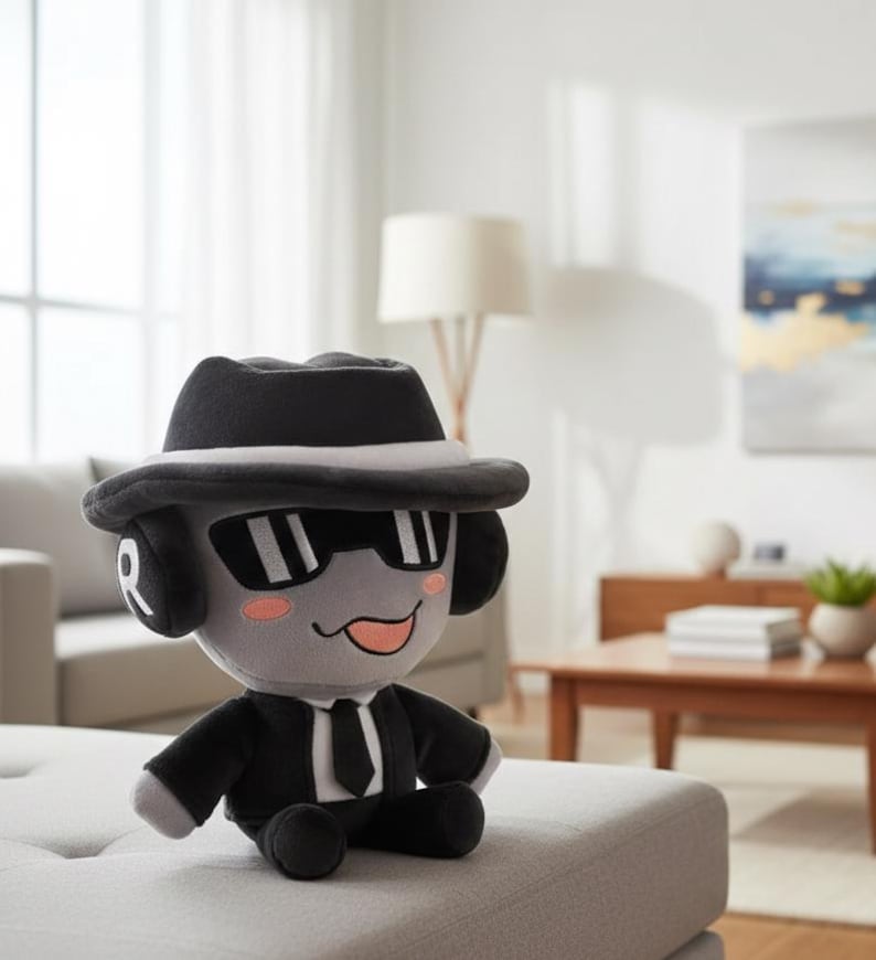 May include: A plush toy in the shape of a cartoon character, wearing a black fedora hat, sunglasses, and a black suit with a tie. The toy has gray skin, pink cheeks, and a smiling expression. The toy is sitting on a gray ottoman.