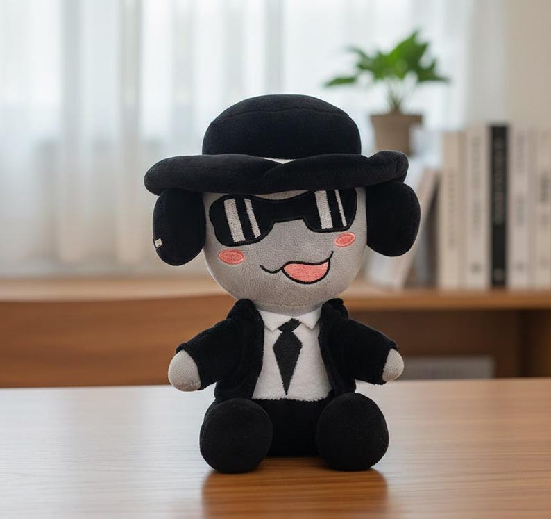 May include: A plush toy dog wearing a black hat, sunglasses, and a suit. The dog has gray fur, black ears, and a pink tongue. The toy is sitting on a wooden surface.