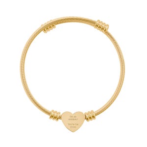 Peut inclure: Un bracelet jonc en fil torsadé doré avec un pendentif central en forme de cœur gravé du texte 'I'm an astronaut, You're the moon'. Le bracelet comporte quatre éléments décoratifs en métal strié placés le long de la tige torsadée.
