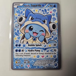 May include: A Poncho Squirtle trading card with 70 HP, featuring a blue character wearing a Blastoise-themed hood. The card displays the attacks Bubble Splash and Hydro Pump, with blue water droplet and shell patterns on the background.
