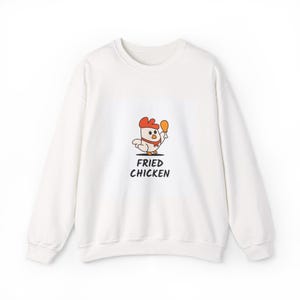 May include: White sweatshirt with a cartoon chicken wearing a chef's hat and holding a fried chicken drumstick. The text "FRIED CHICKEN" is printed below the graphic in black. The sweatshirt has a crew neck and long sleeves.