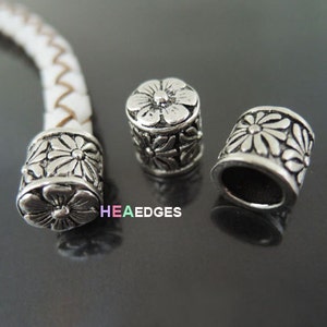 May include: Three silver metal end caps for leather cord bracelets. Each end cap features a floral design.