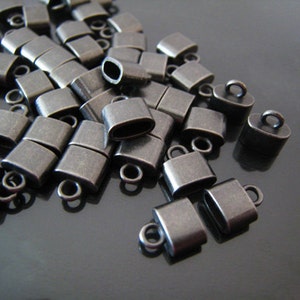 May include: A pile of antique silver-toned metal cord end caps with a small loop on each. The caps are rectangular and have a slightly rounded edge.