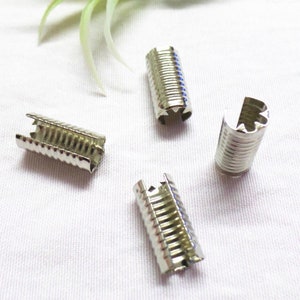 May include: Four silver metal crimp ends for cords or straps. The crimp ends have a ridged design and a star-shaped opening.