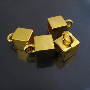 Peut inclure: Quatre embouts en métal de forme cubique dorés avec une boucle sur le dessus. Les embouts sont conçus pour être utilisés dans la fabrication de bijoux.