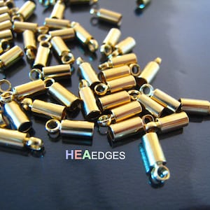 Könnte beinhalten: Ein Haufen goldfarbener Metall-Endkappen für die Schmuckherstellung. Die Endkappen sind zylindrisch mit einer kleinen Schlaufe an einem Ende.