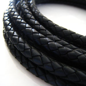 May include: Close-up of black braided leather cord. The cord is woven in a diamond pattern and is coiled in a circle.
