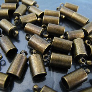 May include: A large group of antique gold-toned metal end caps for cords or jewelry making. The caps have a small loop at the top for attaching to a cord or chain.