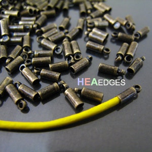 May include: A close-up of a pile of antique gold-toned metal end caps for cord or wire. The end caps have a small loop on one end. A yellow cord is partially visible in the image.