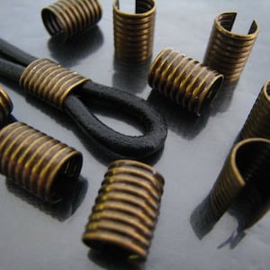 May include: A close-up of a group of gold-toned metal cord end caps. The cord end caps have a ribbed design and are used to finish the ends of cords or straps.