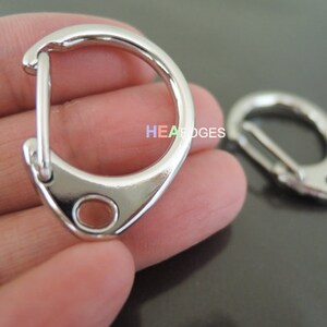 May include: Two silver metal key rings with a swivel clasp. The key rings are in focus and are on a hand.