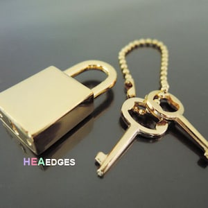 May include: A gold padlock with a key attached to a chain. The padlock and key are both made of metal.