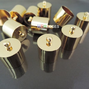 Puede incluir: Un grupo de diez tapones de extremo de metal de color dorado con un pequeño lazo en la parte superior. Los tapones de extremo son de forma cilíndrica y tienen un acabado liso y brillante.