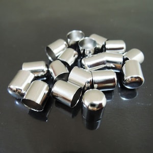 May include: A pile of silver metal end caps for cords or cables. The caps are round and have a smooth, shiny finish.