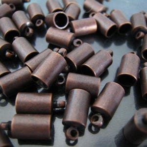 May include: A large group of copper-colored metal end caps for cords or jewelry making. The end caps have a smooth, slightly textured surface and a small loop at the top.