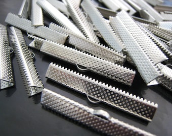 May include: A pile of silver metal clasps with a textured surface and a serrated edge. The clasps are used for attaching fabric or ribbon to create a finished edge.