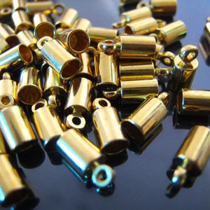 May include: A pile of gold-colored metal end caps for cords or jewelry. The end caps have a small loop on one end and a cylindrical shape.