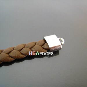 May include: A close-up of a brown braided leather cord with a silver metal end cap and a loop. The cord is about 1/2 inch wide.