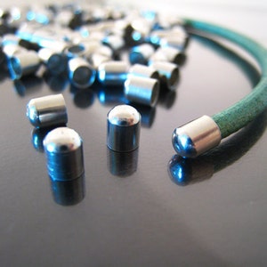 May include: A close-up of silver metal end caps for a leather bracelet. The end caps are round and have a smooth, polished finish. The bracelet is green and is partially visible in the background.
