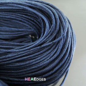May include: Close-up of a reel of dark blue cotton cord. The cord is tightly wound and has a slightly textured surface.