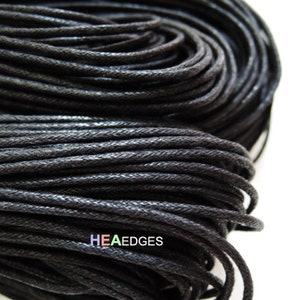 May include: A close-up of a spool of black waxed cotton cord. The cord is tightly wound and has a smooth, polished finish.