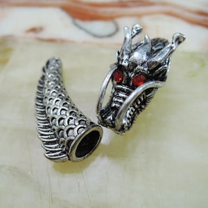 Puede incluir: Encanto de cabeza de dragón plateado con ojos de piedra preciosa roja y un encanto de cola de dragón plateado con un diseño escamoso.