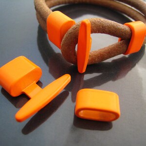May include: Orange leather bracelet with a buckle closure and orange plastic accents. The bracelet is made of two strands of leather and has a simple design.