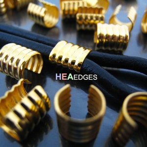 Könnte beinhalten: Goldene Metall-Kordelenden mit geripptem Design. Die Kordelenden sind auf einer schwarzen Lederkordel gezeigt.