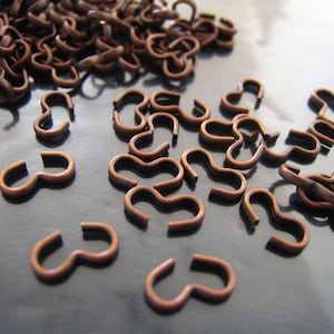 May include: A large pile of copper-colored S-shaped hooks. The hooks are small and have a smooth, shiny finish.