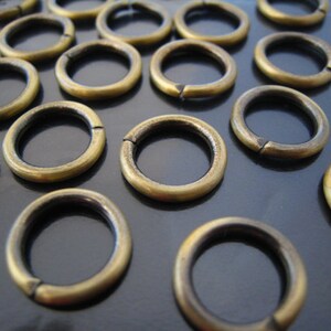 May include: A group of 18 gold-toned metal jump rings. The rings are all the same size and are arranged in a random pattern.