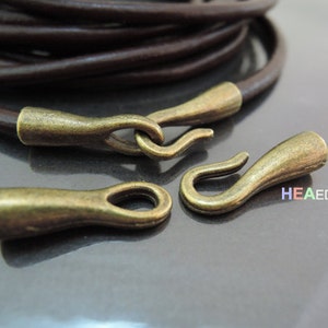 May include: A close-up of brown leather cord with antique brass end caps and a hook clasp. The cord is coiled and the end caps are visible. The text "HEAEDGES" is visible in the background.