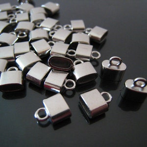 May include: A pile of silver-toned metal end caps with a loop on top. The end caps are square shaped and have a smooth finish.
