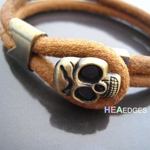 May include: A brown leather bracelet with a gold skull charm. The bracelet is adjustable and has a simple design.