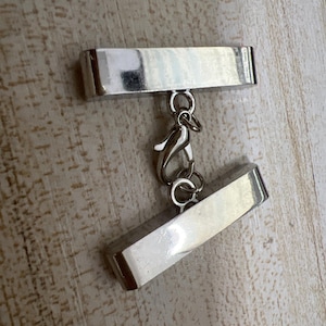 May include: Silver metal clasp with a rectangular shape and a small hook. The clasp is designed to connect two pieces of jewelry or other items.
