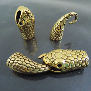 May include: Three gold-colored snake-shaped metal charms. The charms are detailed with a textured snake skin pattern. One charm is a snake head, one is a snake tail, and one is a snake body.