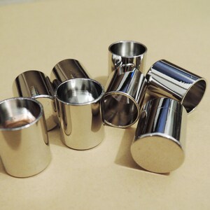 Puede incluir: Un grupo de ocho tapas de metal de color plateado, probablemente para patas de muebles, están esparcidas sobre una superficie de color marrón claro.