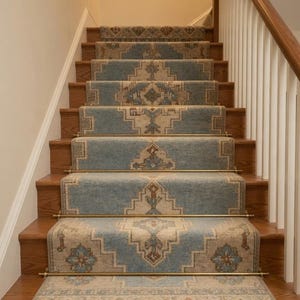 Könnte beinhalten: Eine Holztreppe mit blau-beige gemusterten Teppichläufern. Der Teppich hat ein geometrisches Design mit floralen Akzenten und ist mit Messingstangen befestigt. Die Treppe hat ein weißes Geländer auf der rechten Seite.