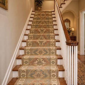 May include: A staircase with a patterned runner rug in shades of beige, red, and blue. The wooden steps are framed by white trim and a dark wood handrail. The walls are a light beige color, and there are decorative sconces.