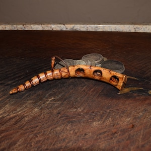 May include: A carved bone whistle with a segmented design and multiple holes. The whistle is curved and has a brown and white color scheme. It is lying on a wooden surface with a pile of silver coins behind it.