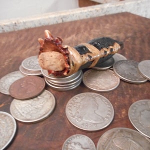 May include: A small, black, leather-wrapped bottle stopper with a cork top and a decorative, brown, wooden base. The stopper is sitting on a pile of silver coins.