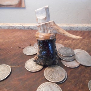 May include: A small, dark brown bottle with a white antler top. The bottle is surrounded by silver coins.