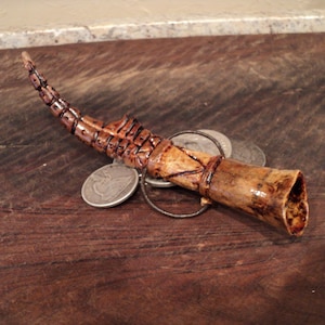 May include: A brown bone whistle with a decorative design, attached to a metal ring with two silver coins.