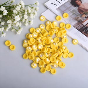 May include: A collection of yellow joystick thumb grips with white paw prints. These grips are designed to enhance the gaming experience and add a touch of style to gaming controllers. The grips are made of a soft, durable material.